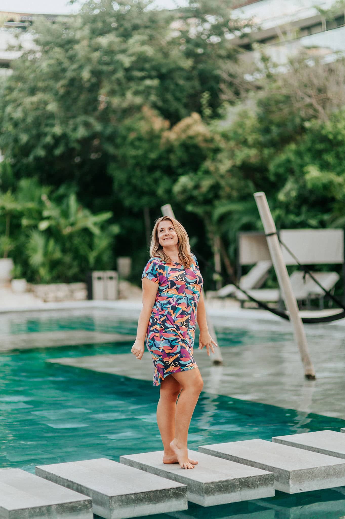 Model in Kip & Boo bamboo nightie standing on bridge steps over a pool with a lush tropical backdrop, showcasing eco-friendly and comfortable bamboo sleepwear.
