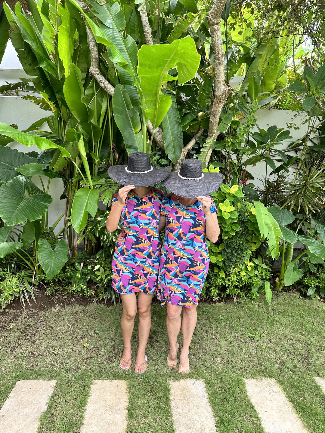 Two women in Bali tropical garden in kip and boo cancun nighties with large black brim hats on